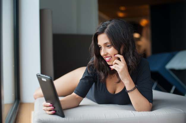 beautiful-sexy-woman-black-bodysuit-lying-mattress-looking-tablet-computer-luxury-resort-blurred-background_10069-677